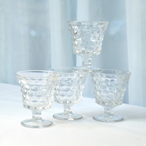 May include: Four clear glass goblets with a diamond pattern. The goblets have a short stem and a round base.