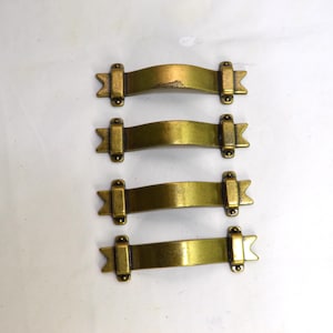 May include: A set of four brass-toned metal drawer pulls arranged vertically. Each pull features a curved central handle with rectangular mounting plates at both ends, finished with pointed, arrow-like decorative tips on the outer edges.