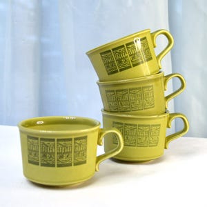 May include: A stack of four green ceramic mugs with a geometric pattern. The mugs are stacked on a white surface.