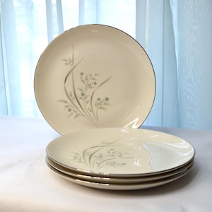 May include: Three white dinner plates with a delicate floral design in shades of blue and silver. The plates have a gold rim.