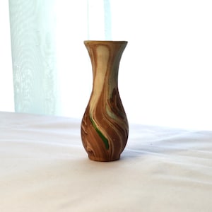 May include: A small, brown and green ceramic vase with a marbled design. The vase has a narrow neck and a rounded base.