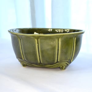 May include: A green ceramic planter with a fluted design and three feet. The planter is oval shaped and has a glossy finish.