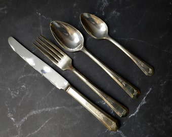 May include: A set of silver flatware, including a fork, knife, and two spoons, laid out on a black marble surface.