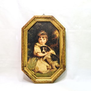 May include: An octagonal framed painting featuring a child with light brown hair wearing a cream-colored garment, embracing a black and white dog. The frame is ornate, textured, and gold-colored, with a small metal hanging loop at the top center.