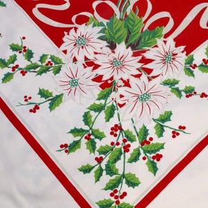 May include: A white tablecloth featuring a festive holiday print with a large red corner section, white ribbons, and a central cluster of white poinsettia flowers surrounded by green holly leaves and small red berries along the borders.