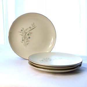 May include: Set of four white ceramic dinner plates with a delicate floral design in shades of blue and green. The plates have a gold rim.