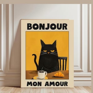 Puede incluir: Un cuadro enmarcado con un gato negro sentado en una mesa con café y un cruasán. Las palabras "BONJOUR MON AMOUR" están impresas en negrita encima y debajo de la ilustración del gato, sobre un fondo amarillo.