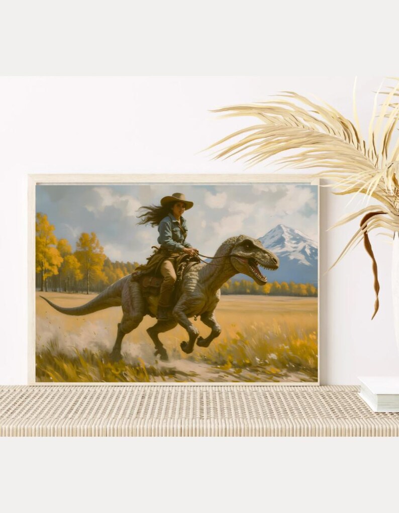 May include: A framed art print depicts a person riding a dinosaur through a field. The person wears a cowboy hat and denim shirt. The dinosaur is gray and brown. The background features a mountain and yellow trees.