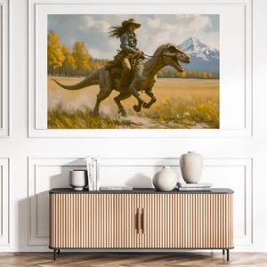 May include: A framed art print depicts a person riding a dinosaur through a field. The person wears a cowboy hat and denim shirt. The dinosaur is gray and brown. The background features a mountain, trees, and a yellow field.