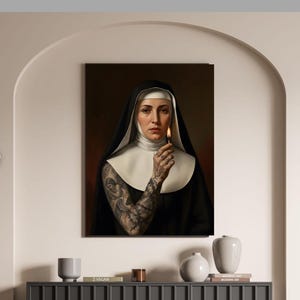 May include: A framed portrait of a nun in a black habit and white wimple, holding a lit match. The nun has a full sleeve tattoo on her arm. The background is a dark red. The portrait is hanging on a beige wall.