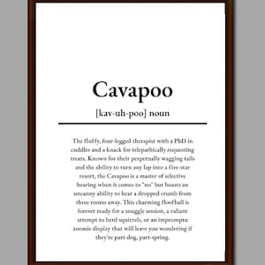 May include: A framed print defining "Cavapoo." The text describes the Cavapoo as a fluffy, four-legged therapist. The print is in a dark brown frame, with black text on a white background. The definition includes the pronunciation.