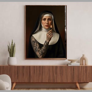 May include: A framed portrait of a nun holding a lit match. The nun is wearing a traditional black habit with a white wimple and collar. Her arm is covered in intricate tattoos. The artwork is displayed on a wooden cabinet.