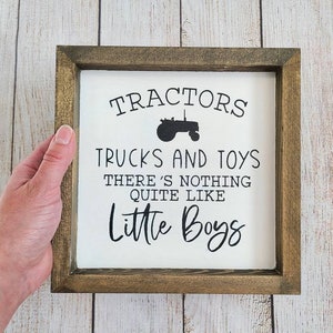 Puede incluir: Letrero cuadrado con marco de madera con el texto "Tractors, Trucks and Toys, There's Nothing Quite Like Little Boys" en letras negras. El letrero tiene un fondo blanco y un marco marr&oacute;n oscuro.