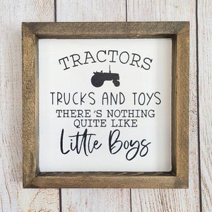 Puede incluir: Un letrero enmarcado con fondo blanco y texto negro. El texto dice: "Tractores, camiones y juguetes, no hay nada como los ni&ntilde;os peque&ntilde;os". Un gr&aacute;fico de tractor negro est&aacute; encima del texto. El marco es de color marr&oacute;n oscuro.