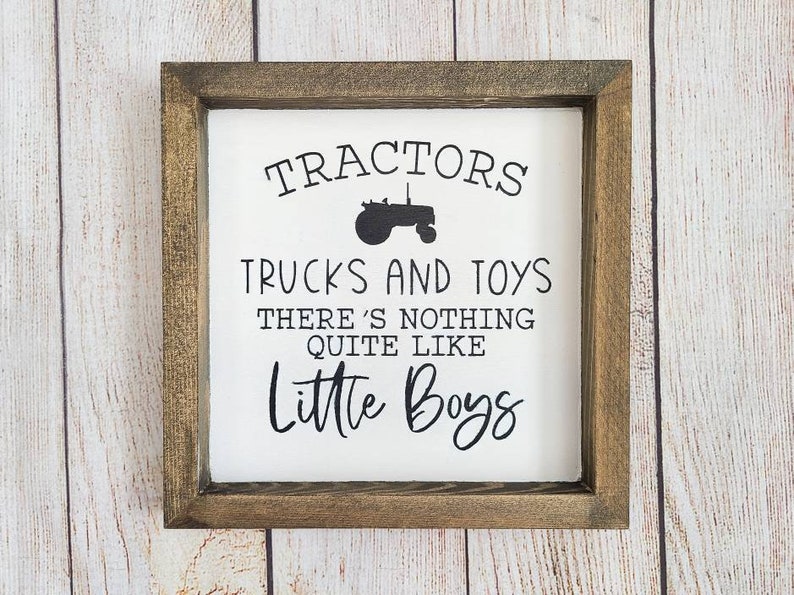 Puede incluir: Un letrero enmarcado con fondo blanco y texto negro. El texto dice: "Tractores, camiones y juguetes, no hay nada como los ni&ntilde;os peque&ntilde;os". Un gr&aacute;fico de tractor negro est&aacute; encima del texto. El marco es de color marr&oacute;n oscuro.