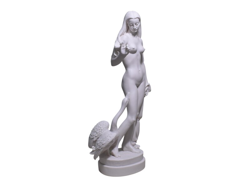 May include: White marble statue of a woman standing with a swan. The woman is nude and has long hair. The swan is positioned behind her, with its neck wrapped around her leg.