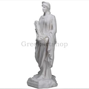 May include: A white marble statue of Demeter, the Greek goddess of agriculture. She is depicted in flowing robes, holding a basket of fruits and wheat. The statue has the text "Demeter" at the base and the text "Greekartshop" in the background.