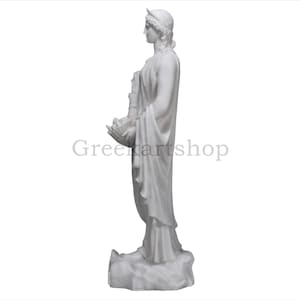 May include: A white marble statue of a classical figure, seen in profile, holding an object. The figure wears a draped garment and a headpiece. The statue is on a white background. The text "Greenartshop" is visible.