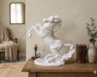 Puede incluir: Una estatua de caballo de cerámica blanca encabritada sobre sus patas traseras. La escultura está sobre una mesa de madera con un candelabro, libros y un jarrón. El fondo incluye una silla, un espejo y una alfombra.