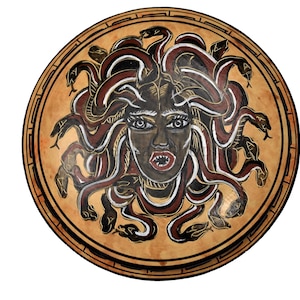 Pode incluir: Um escudo redondo de madeira com uma imagem pintada de Medusa, uma figura mitológica grega com cobras no cabelo, uma expressão feroz e um design vermelho e branco.