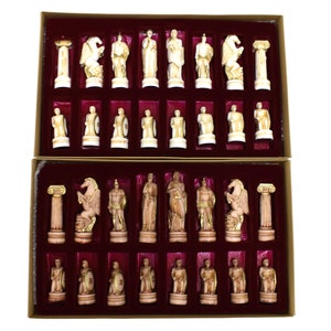 May include: A complete chess set featuring ivory-colored pieces with gold accents, presented in a two-tiered box with a burgundy velvet interior. The chess pieces depict classical figures and architectural elements.