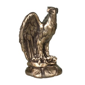 Pode incluir: Uma estatueta de &aacute;guia na cor bronze sobre uma base de rocha texturizada. A &aacute;guia &eacute; representada de perfil com as asas parcialmente abertas, exibindo texturas detalhadas nas penas e um bico afiado, com um acabamento de brilho met&aacute;lico.