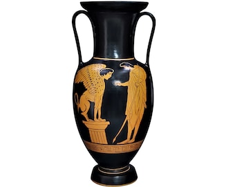 May include: A black ceramic amphora vase featuring two handles and a wide rim. The body is decorated with orange-toned illustrations of a winged sphinx perched on a pedestal facing a figure holding a staff, with a Greek key pattern at the base.