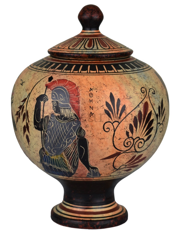 May include: A ceramic Greek urn with a lid, decorated with a black-figure painting of a warrior holding a spear. The urn is painted in shades of red, black, white, and yellow. The urn has a round body and a tall, slender base. The urn is decorated with a floral pattern and the word "ATHENA" in Greek.