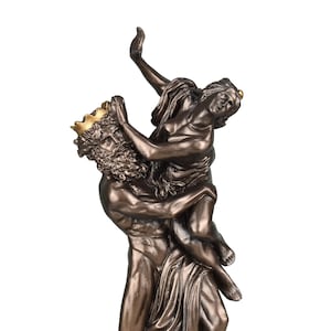 Może przedstawiać: Brązowa statua przedstawiająca muskularną postać niosącą kobietę. Mężczyzna nosi złotą koronę i ma długą brodę. Kobieta jest odziana w powiewającą tkaninę, z uniesioną ręką. Temat klasyczny.