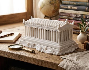 May include: A white architectural model of a classical temple with columns, set on a wooden surface. A magnifying glass, books, and a globe are nearby. The model is a detailed replica of a historical building.