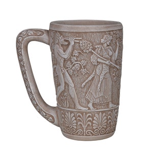 Puede incluir: Una taza de cerámica con un esmalte beige y un diseño en relieve blanco que representa una escena de la mitología griega. El diseño presenta dos figuras, un hombre y una mujer, con detalles intrincados y motivos florales.