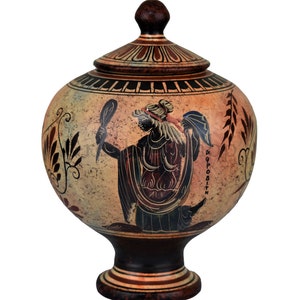 May include: A brown ceramic Greek style urn with a lid. The urn is decorated with a black and white image of a woman holding a mirror. The text "APHRODITE" is written on the urn.