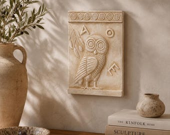 May include: A rectangular beige wall plaque featuring a relief carving of an owl, an olive branch, and the Greek letters Alpha, Omicron, and Epsilon. The plaque has a decorative spiral border at the top and bottom, with a matte, stone-like finish.