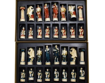 May include: A complete chess set featuring intricately detailed pieces. The pieces are in a Roman theme, with figures in red, blue, and gold. The set is displayed in a black box with individual compartments for each piece.
