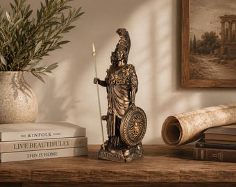 May include: A bronze-colored Athena statue holding a spear and shield. The statue is on a wooden surface, with books and a vase of greenery nearby. The word "ATHENA" is at the base of the statue.