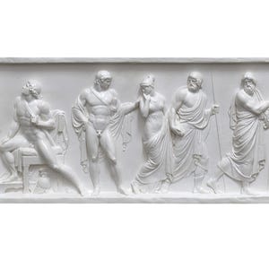 Puede incluir: Una escultura en relieve de yeso blanco que representa a cinco figuras con vestimenta clásica. Las figuras están dispuestas en línea, con las dos figuras de la izquierda sentadas y las tres figuras de la derecha de pie. La escultura está colocada sobre un fondo blanco.