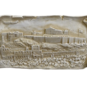 May include: A white plaster relief sculpture depicting the Acropolis in Athens, Greece. The sculpture is in the shape of a scroll with a Greek flag at the top.