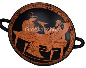 May include: Black-figure pottery bowl with two figures, a woman offering a plate of food to a seated man. The bowl has a red-orange background and a black geometric border.