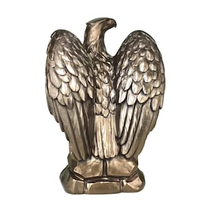 Pode incluir: Uma est&aacute;tua de &aacute;guia na cor bronze sobre uma base rochosa. A &aacute;guia &eacute; representada com as asas parcialmente abertas, exibindo texturas detalhadas de penas por todo o corpo. A cabe&ccedil;a est&aacute; voltada para a direita e o acabamento &eacute; met&aacute;lico.