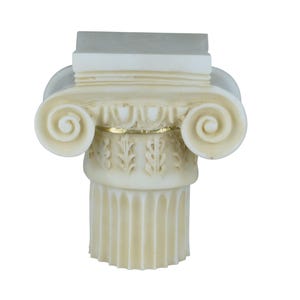 Pode incluir: Um capitel jónico decorativo creme. O capitel apresenta um topo retangular, volutas enroladas e entalhes detalhados. Uma faixa dourada acentua o design. É um elemento arquitetónico clássico.