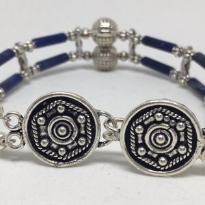 May include: A silver bracelet with blue beads and two round silver charms. The charms have a circular design with a center circle and smaller circles around it.