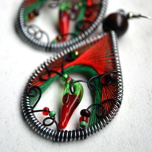 Può includere: Un paio di orecchini rossi e verdi con un design a forma di peperoncino. Gli orecchini sono realizzati in filo e perline e hanno una finitura argentata.