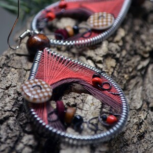 May include: A pair of red and brown earrings with metal wire and fabric. The earrings feature a brown wooden bead, a red and white checkered button, and a red and white polka dot button.
