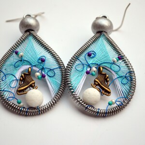 May include: A pair of teardrop-shaped earrings with a winter theme. Each earring features a white and blue wire wrapped design with a small white bead, a bronze ice skate charm, and a silver hook.