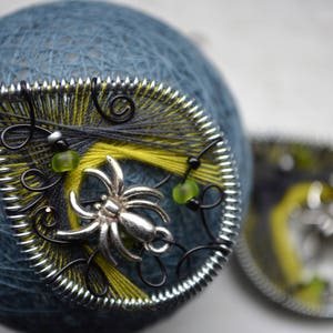 May include: A pair of silver and black earrings with a spider web design and green beads. The earrings are made with wire and thread.