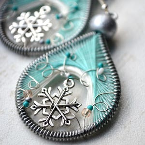 Puede incluir: Un par de pendientes en forma de lágrima de color turquesa y blanco con abalorios de copo de nieve plateados y cuentas.