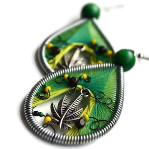 Könnte beinhalten: Ein Paar grüne und gelbe Ohrringe mit einem silbernen Blattanhänger. Die Ohrringe sind aus Draht und Garn gefertigt und haben ein Perlmuster.