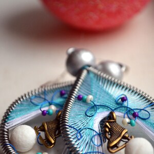 May include: A pair of handmade earrings featuring a blue, white, and silver wire design with a small ice skate charm and white beads. The earrings are a winter-themed design.