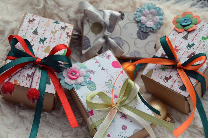 May include: Five small gift boxes wrapped in festive paper with colorful ribbons and bows. The boxes are decorated with various holiday themes, including reindeer, Christmas trees, and snowflakes.