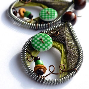 Puede incluir: Un par de pendientes de alambre envueltos en verde y marrón con un botón blanco y cuentas marrones.